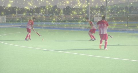 Executing quick passes field hockey players in red-striped jerseys moving on green turf