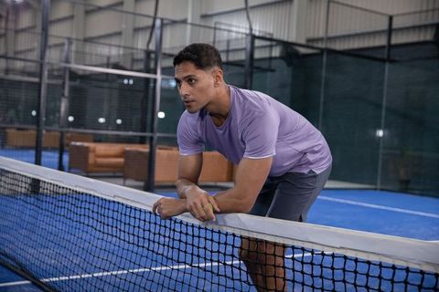 Man leaning on net holding ball on indoor blue court, showing focus and intensity
