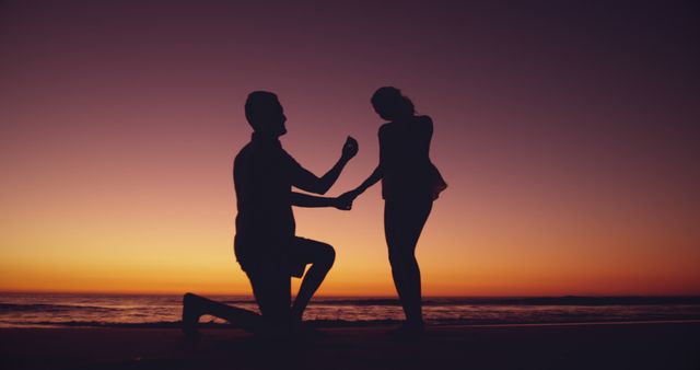 Silhouetted couple on the beach at sunset, with copy space. Their romantic proposal moment is set against a breathtaking outdoor backdrop.