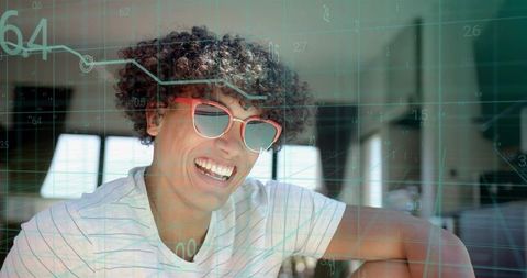 Smiling man wearing red sunglasses and striped tee in sunlit workspace with data overlay