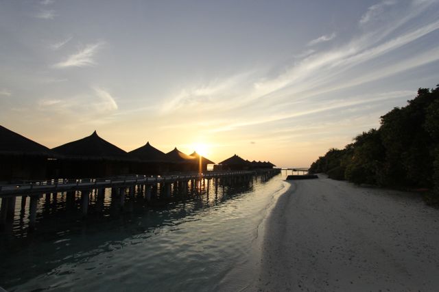 Beautiful sunset in a tropical paradise with luxurious overwater bungalows in background and serene beach on foreground. Perfect for travel brochures, vacation advertisements, websites promoting exotic escapes, and social media posts inspiring wanderlust.