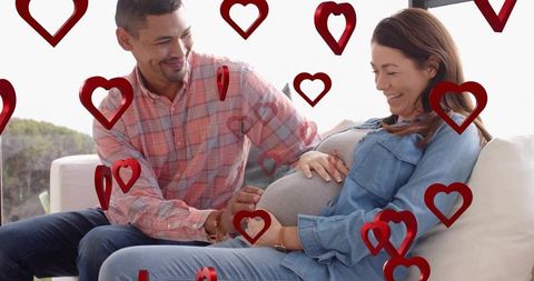 Expectant couple sharing tender sunlit moment on couch, father smiling touching belly