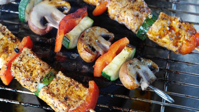 Vegetable and chicken skewers grilling on a barbecue with mushrooms, zucchini, bell peppers. Bright and appetizing close-up showcasing the perfect cookout food. Suitable for outdoor cooking promotions, healthy eating articles, summer barbecue advertisements, or recipe blogs.