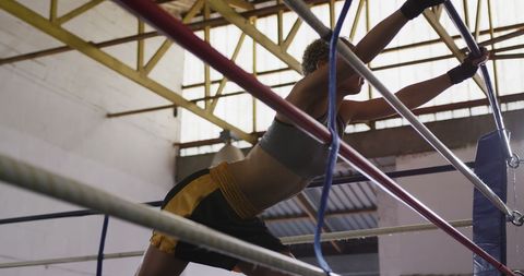 Female boxer stretching on boxing ring ropes in gym