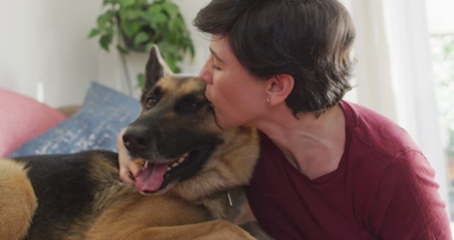 This image shows an owner embracing and kissing their German Shepherd while sitting on a sofa. It is ideal for use in campaigns promoting pet adoption, veterinary services, pet care products, or content related to pet-owner relationships and the joy of having pets.