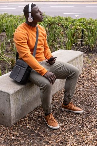 Urban commuter sitting on concrete bench listening to music with headphones and smartphone