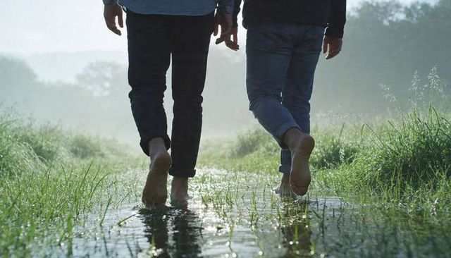 Barefoot walking through misty meadow puddle at dawn, wet jeans and reflective water