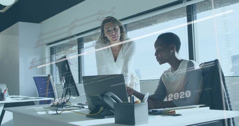 Two Female Professionals Collaborating Over Code on Laptop and Monitor in Bright Office