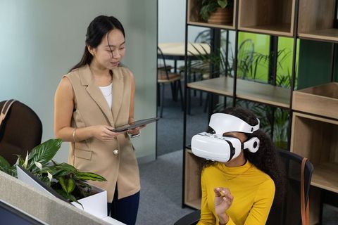 Coworkers testing virtual reality headset in modern office while monitoring on tablet