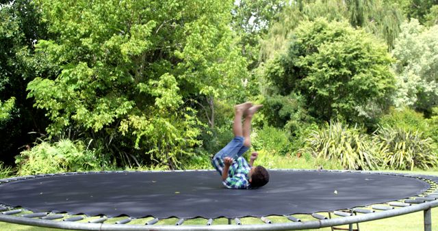Boy playing on trampoline surrounded by green trees and foliage, enjoying outdoor activity on a sunny day. Useful for themes related to childhood, outdoor fun, recreational activities, and family time. Ideal for health and wellness campaigns, lifestyle blogs, and promotions for outdoor toys or gear.