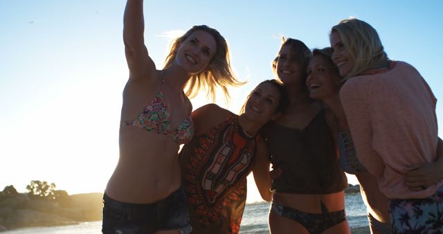 Group of female friends takes selfie on beach during sunset. Perfect for summer vacation themes, promotions about friendship, or outdoor activities. Can be used in travel brochures, lifestyle blogs, or social media posts featuring happiness and bonding.