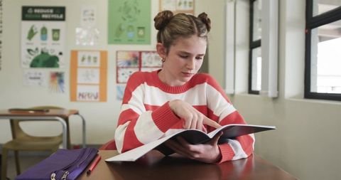 Preteen Girl Reading Textbook in Classroom, Focused Student Learning