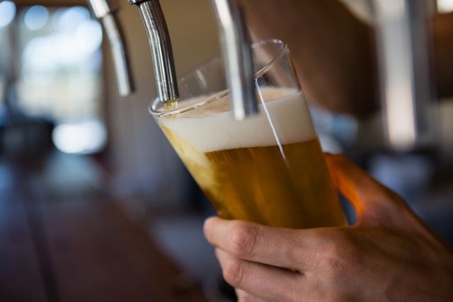 Cropped hand of bartender pouring beer from tap in glass at restaurant