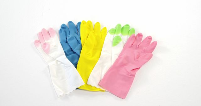 Five rubber cleaning gloves in various colors (pink, green, yellow, white, blue) neatly arranged on white background. Perfect for illustrating sanitation, household chores, and multi-colored cleaning supplies. Ideal for advertising cleaning products, articles about effective house cleaning, or visuals for hygiene practices.