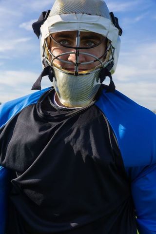 Lacrosse goalie standing confidently on field with gear under blue sky