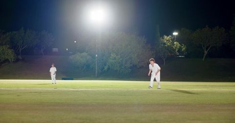 Two cricketers fielding under floodlights on outfield at night with copy space