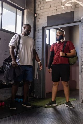 Laughing friends meeting at gym entrance carrying duffel bags and headphones