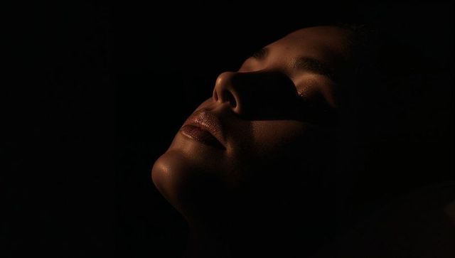 Tilting female face into warm chiaroscuro light for moody low-key beauty portrait