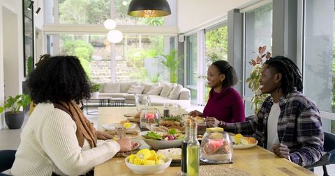 Black Friends Sharing Casual Lunch at Wooden Dining Table in Sunlit Modern Open-Plan Home