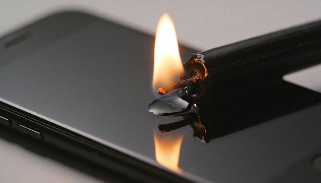 Charred candle flame melting wax on glossy smartphone screen with fire reflection
