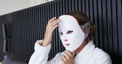 Woman wearing led facial mask in white bathrobe practicing at-home skincare and relaxation