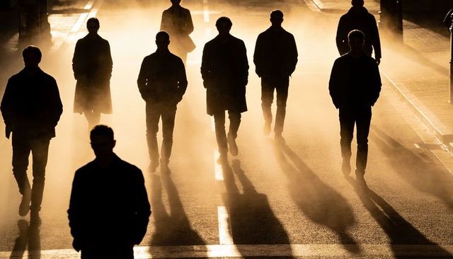 Walking backlit silhouettes crossing misty urban street at sunrise casting dramatic long shadows