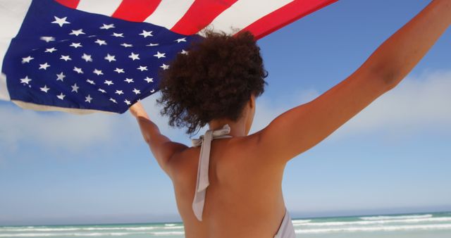 Image showing an African American woman holding an American flag on a beach. Suitable for celebrating Independence Day, promoting patriotism, beach vacations, summer activities, and cultural diversity. Perfect for articles and campaigns about American holidays and freedom.