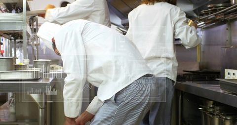 Bending chef reaching lower shelf in busy stainless steel kitchen with data overlay