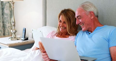 Happy Senior Couple Relaxing with Laptop in Bedroom