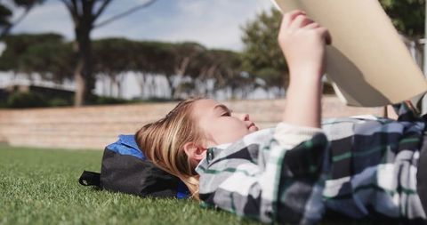 Young girl relaxing outdoors reading sketchpad on lawn
