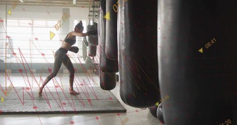 Female boxer training on heavy bag in industrial gym with digital performance overlay