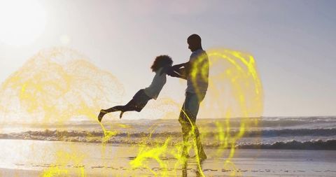 Father swinging daughter on beach at sunset with golden glow and wet-sand reflections