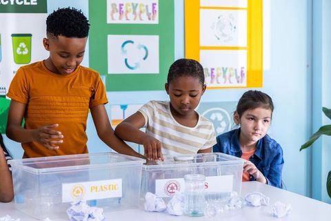 Multiracial children sorting recyclables in classroom teaching sustainability and teamwork