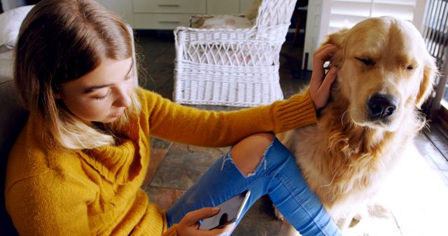 Young woman in yellow sweater petting golden retriever while sitting on floor in cozy living room. Ideal for use in advertisements promoting pet products, lifestyle blogs about pet ownership, or social media posts emphasizing the bond between humans and dogs. Perfect for content related to relaxation at home, friendship, and pet care tips.