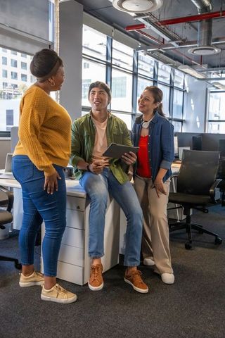 Diverse coworkers collaborating and smiling in modern open-plan office with tablet