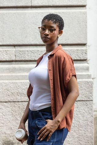 Confident african woman holding coffee wearing glasses and rust shirt on urban street
