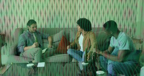 Three friends chatting on sofa holding beer bottles and notes casual home hangout