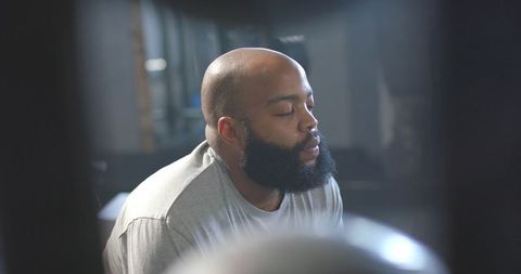Bearded man resting between sets in gym, soft directional light highlighting quiet focus