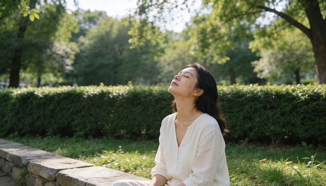 Young woman relaxing in sunlit park sitting on stone ledge with peaceful expression