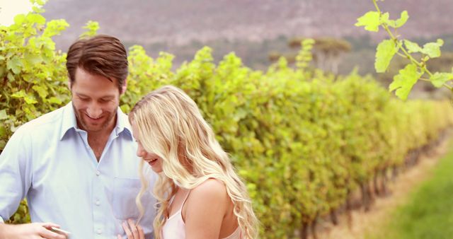A young Caucasian couple enjoys a moment together in a vineyard, with copy space. Their smiles suggest a casual, romantic outing amidst the rows of grapevines.