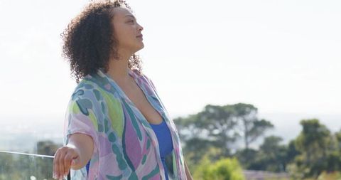 African american woman standing on glass balcony wearing pastel wrap looking at horizon