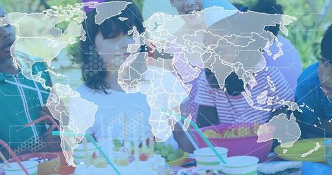 Children celebrating outdoor birthday picnic with cake, snacks and world map tech overlay