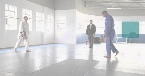 Athlete stepping in blue gi across bright dojo mats with coach observing