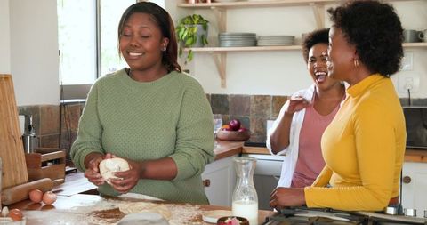 Joyful friends kneading dough in warm kitchen