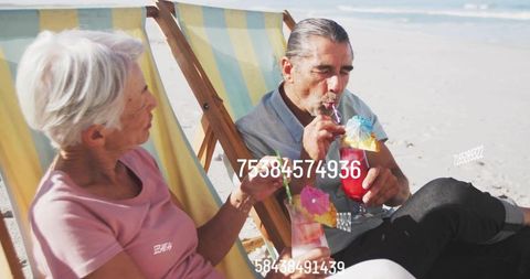 Senior couple sipping cocktails on sunny beach chairs, relaxing and showing white numbers