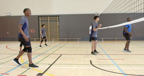 Diverse male volleyball team practicing on indoor gym court with african american player