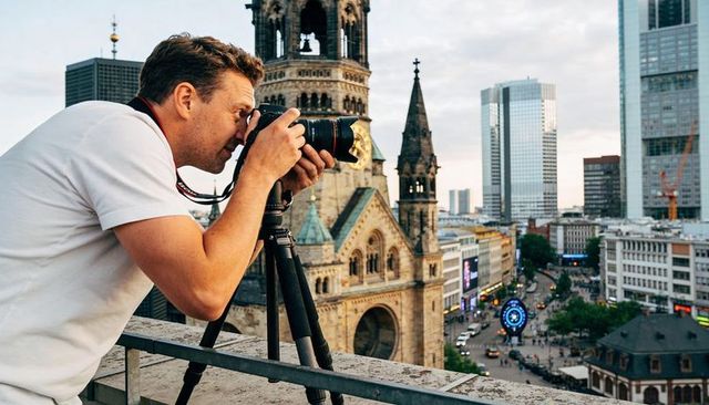 Rooftop photographer shooting cathedral cityscape with dslr tripod in evening light