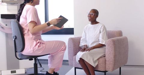 Clinician discussing care with seated patient in medical gown using tablet for consultation