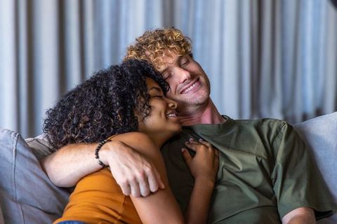 Interracial couple cuddling on sofa embracing cozy home romance warm intimacy smiling