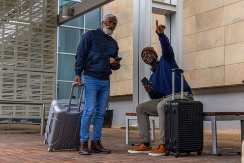Multigenerational travelers checking phones pointing at transit station with suitcases